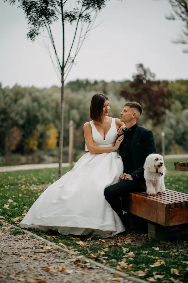 Rebeka és Martin: A pár a fapadon ül kis fehér kutyájával.