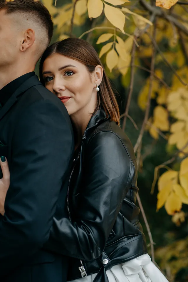 Rebeka és Martin: A menyasszony hátulról átöleli a vőlegényt az őszi lombok alatt.