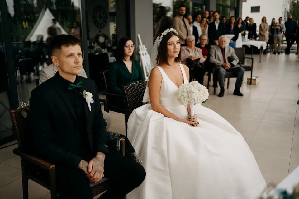 Rebeka és Martin: A pár ülve hallgatja a szertartást a vendégek előtt.