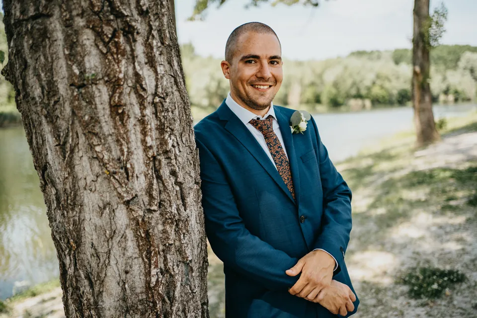 Albert mosolyogva támaszkodik egy fának